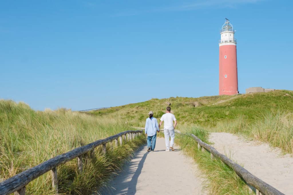 Wandelen mensen in de duinen met een vuurtoren op de achtergrond